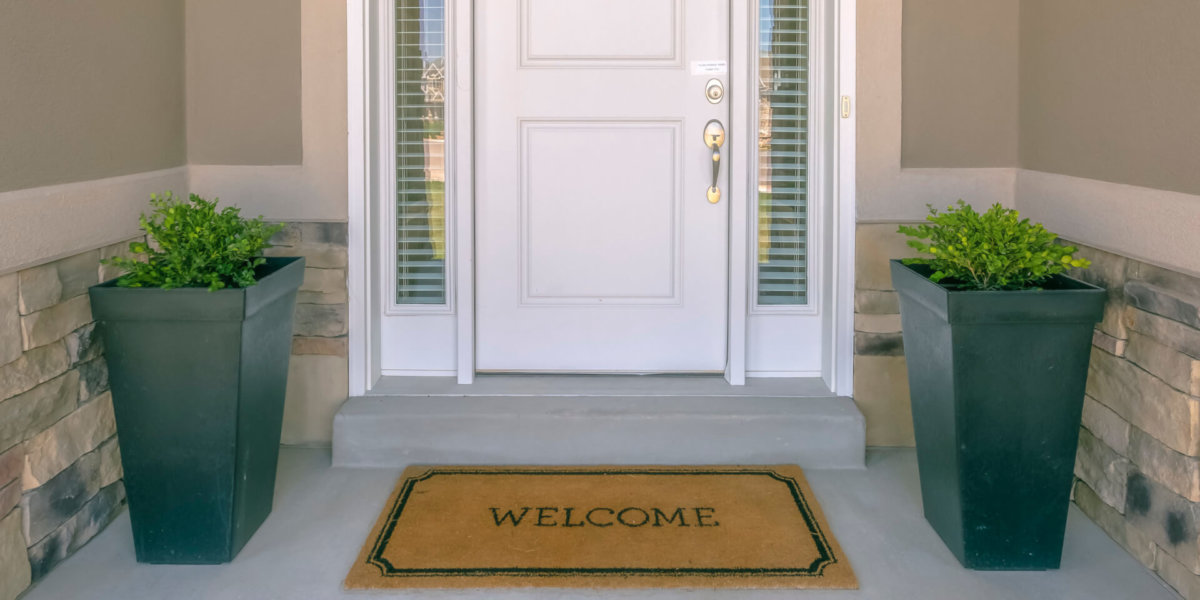 Front door with welcome mat and potted plants