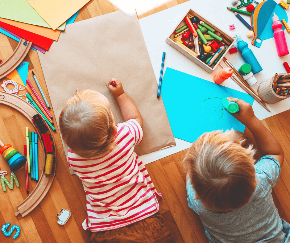 Two young children lying on the floor coloring with crayons