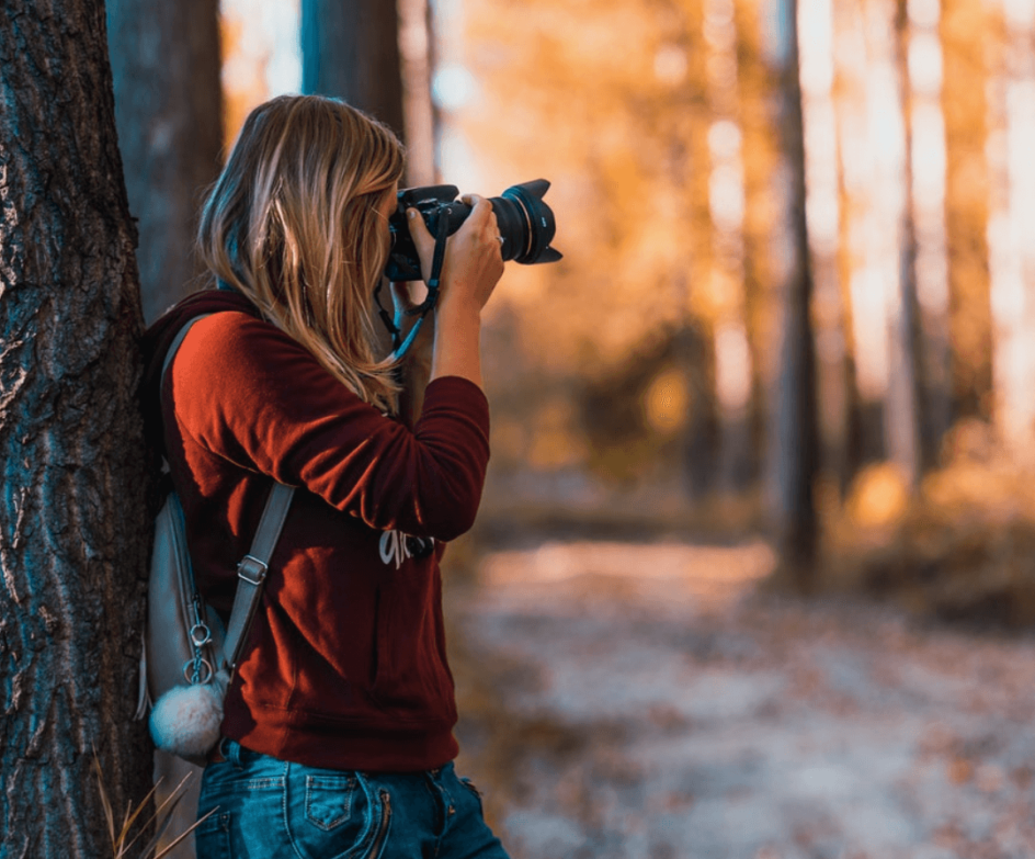 Photo of woman taking a photo with a DSLR camera in a forest. Photo credit: David Bartus