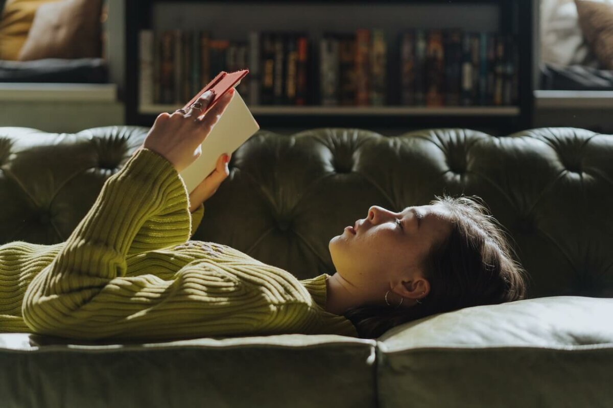 Woman laying on a sofa reading a book. Image credit: cottonbro