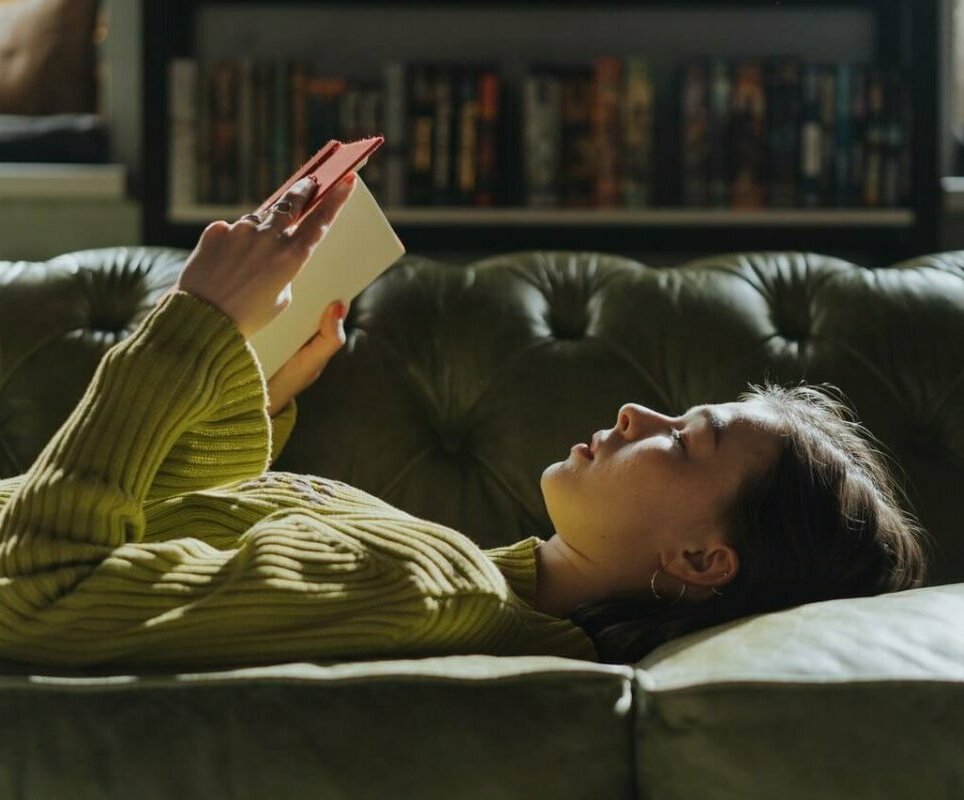 Woman laying on a sofa reading a book. Image credit: cottonbro