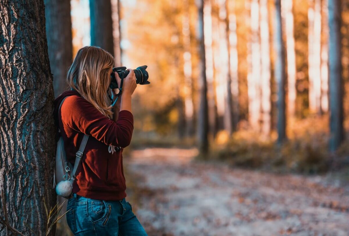 Photo of woman taking a photo with a DSLR camera in a forest. Photo credit: David Bartus